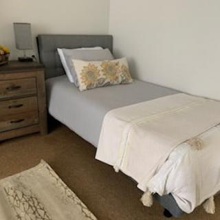 A minimalist bedroom featuring a neatly made bed with gray bedding and a decorative pillow, adjacent to a wooden nightstand.