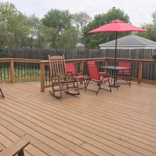 A spacious wooden deck featuring a dining set with an umbrella and two rocking chairs.