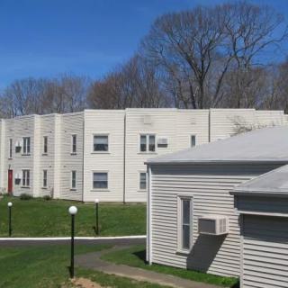 Residential apartment buildings with a grassy lawn and trees in the background.