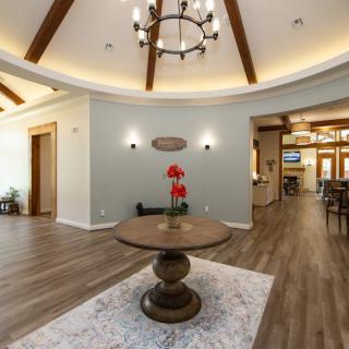 A modern lobby featuring a round wooden table, chandelier, and decorative vase under elegant wooden beams.