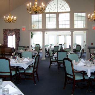 A well-lit dining room with neatly arranged tables and chairs, featuring large windows and chandeliers.