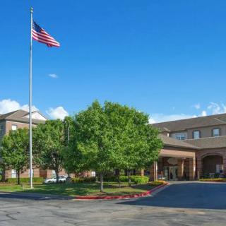 A building with an American flag, surrounded by trees and a parking lot under a clear blue sky.