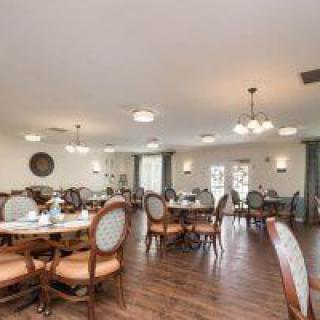 A spacious dining room with neatly arranged tables and chairs, featuring elegant lighting and a wooden floor.