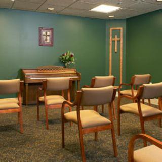 A small chapel with seating and an organ against a green wall featuring a cross.