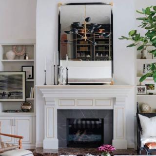 A stylish living room featuring a fireplace with a large mirror above it, flanked by built-in bookshelves and decorated with plants.