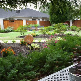 A beautifully landscaped garden with various flowers and greenery, enclosed by a wooden fence.