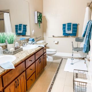 A modern and neatly organized bathroom with wooden cabinets, a large mirror, and blue towels.