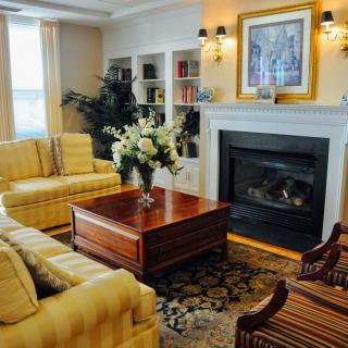A cozy living room featuring a fireplace, yellow sofas, and a wooden coffee table adorned with flowers.