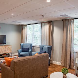 A cozy living room with plush seating and a television, featuring large windows and elegant curtains.