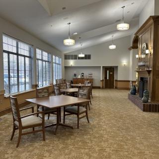 A spacious, carpeted room with tables and chairs, large windows, and a fireplace.