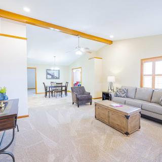 A bright and spacious living room with neutral tones, featuring a comfortable sofa, armchair, and a view into the dining area.