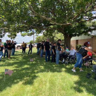 A group gathering under a tree, featuring individuals and wheelchairs, with small flags placed on the grass.