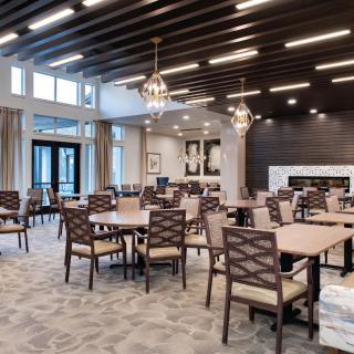 A modern dining area with arranged tables and chairs, featuring elegant lighting and large windows.