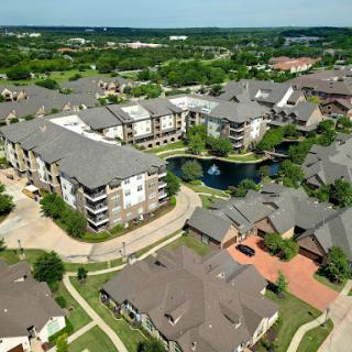 Aerial view of a modern apartment complex surrounded by green landscapes and a serene water feature.