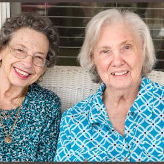 Two elderly women sitting together, smiling warmly.