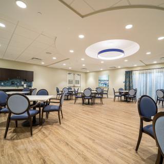 A modern dining room with neatly arranged tables and chairs, featuring elegant lighting and a wooden floor.