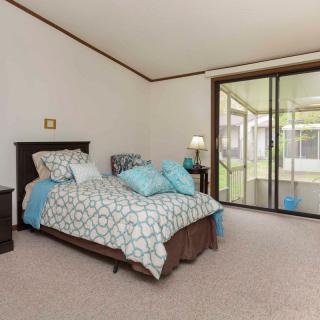 A cozy bedroom with a neatly made bed, featuring blue and white bedding, a bedside lamp, and sliding glass doors leading to a patio.