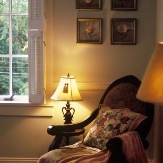 A cozy living room corner with a lamp, chair, and window.