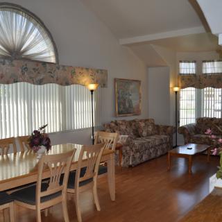 A cozy living and dining area with elegant wood flooring, featuring a dining table and comfortable sofas near large windows.