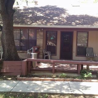 A cozy house with a shaded porch and seating area under a large tree.