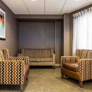 A modern waiting room with patterned chairs and a sofa, featuring soft lighting and neutral colors.