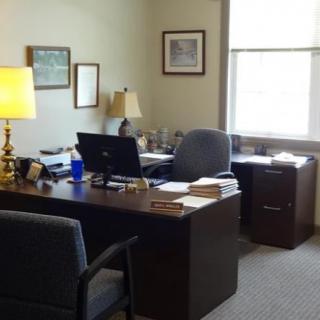A tidy office with a desk, computer, chair, and lamp near a window.
