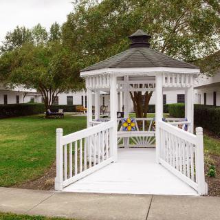A white gazebo sits in a grassy outdoor area surrounded by trees and pathways.