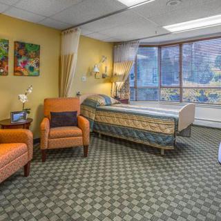 A cozy hospital room with a bed, chairs, and large windows letting in natural light.