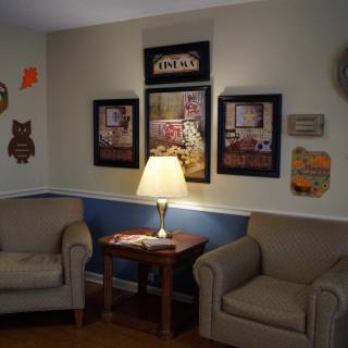 A cozy living room with two armchairs, a lamp on a wooden side table, and decorative wall art.