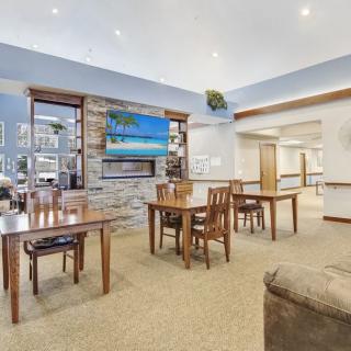 A cozy dining area with wooden tables and chairs, featuring a fireplace and a wall-mounted television.