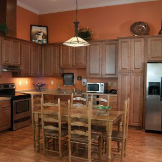 A warm and inviting kitchen with wooden cabinets, a dining table, stainless steel appliances, and orange walls.