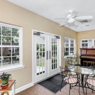 A bright sunroom features a dining set, piano, and large glass doors leading to the garden.
