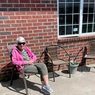 A person sits outside on a chair, enjoying the sunny weather next to a brick wall.