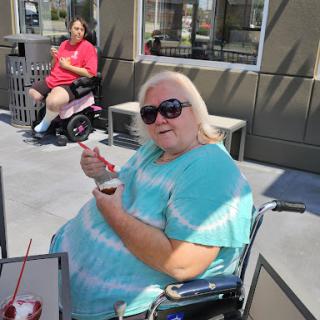A woman enjoying a treat outdoors while seated in her wheelchair.