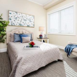 A cozy and elegantly decorated bedroom with a neatly made bed, artwork on the wall, plant, and natural light streaming through the window.