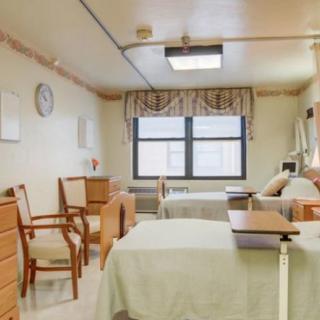 A clean and organized hospital room with two beds, chairs, and a window with curtains.