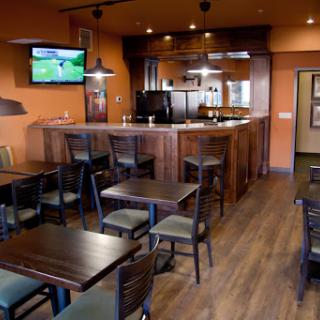 A cozy dining area showcasing wooden tables and chairs, with a bar in the background and sports on the TV.