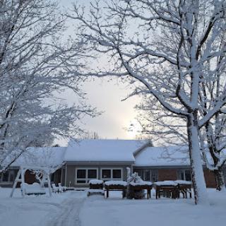 A peaceful winter scene with a snow-covered house surrounded by bare trees.