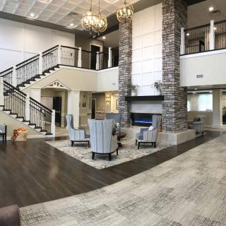 A spacious and elegant lobby featuring a grand staircase, comfortable seating area, and a central fireplace.