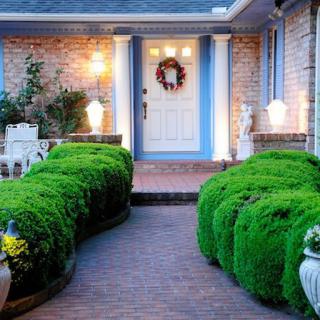 A welcoming front entrance with well-maintained shrubs, a wreath on the door, and warm outdoor lighting along a brick pathway.