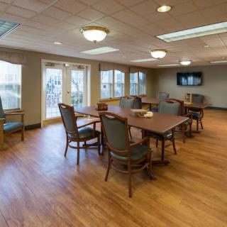 A spacious community dining area with wooden floors and ample natural light from large windows.