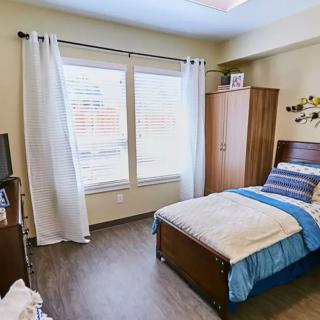 A cozy bedroom with a single bed, wardrobe, and large windows letting in natural light.