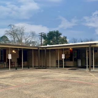 An exterior view of a commercial building with a spacious parking lot, surrounded by trees under a cloudy sky.