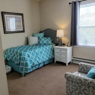 A cozy bedroom with teal bedding, a nightstand, and an armchair by the window.