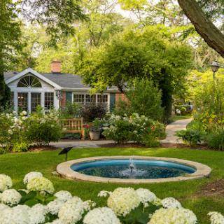 A serene garden scene featuring a charming house, vibrant flowers, and a peaceful water feature.