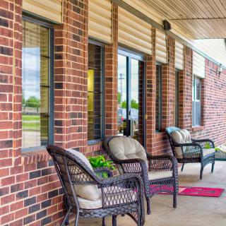 A cozy porch with wicker chairs, cushions, and a red doormat against a brick wall.