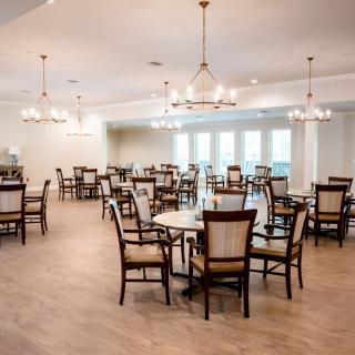 A spacious dining room with multiple tables and chairs, illuminated by elegant chandeliers.