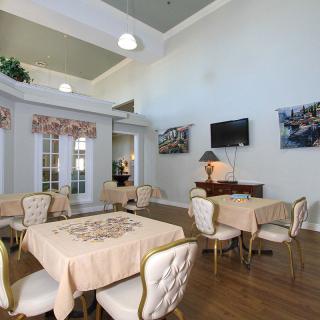 A well-decorated dining area with elegant tables and chairs, featuring a television and lamps on wooden flooring.