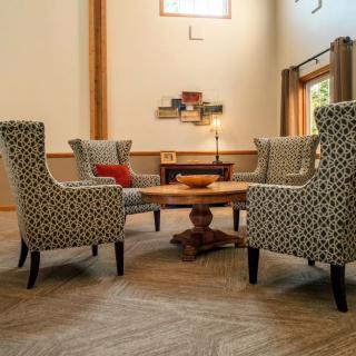 A modern living room with patterned armchairs surrounding a wooden coffee table, featuring neutral tones and wood flooring.