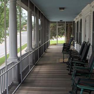 A serene screened porch with rocking chairs and columns overlooking a green lawn.